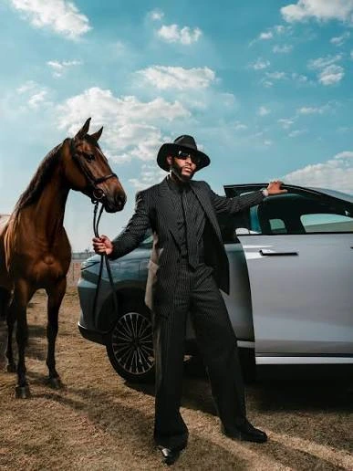 Stylish man in a black suit stands beside a horse and luxury SUV.